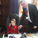 young student sat in their headteacher's chair, taking a phone call