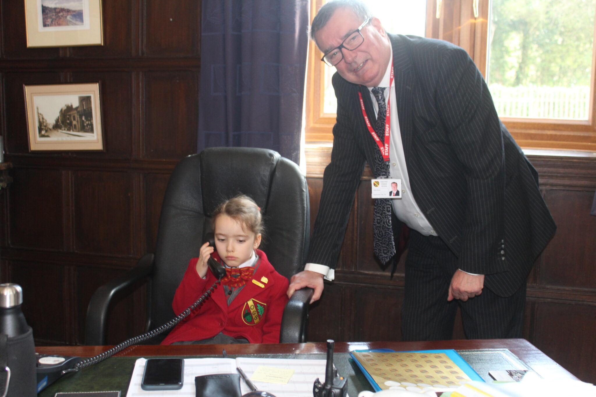 young student sat in their headteacher's chair, taking a phone call